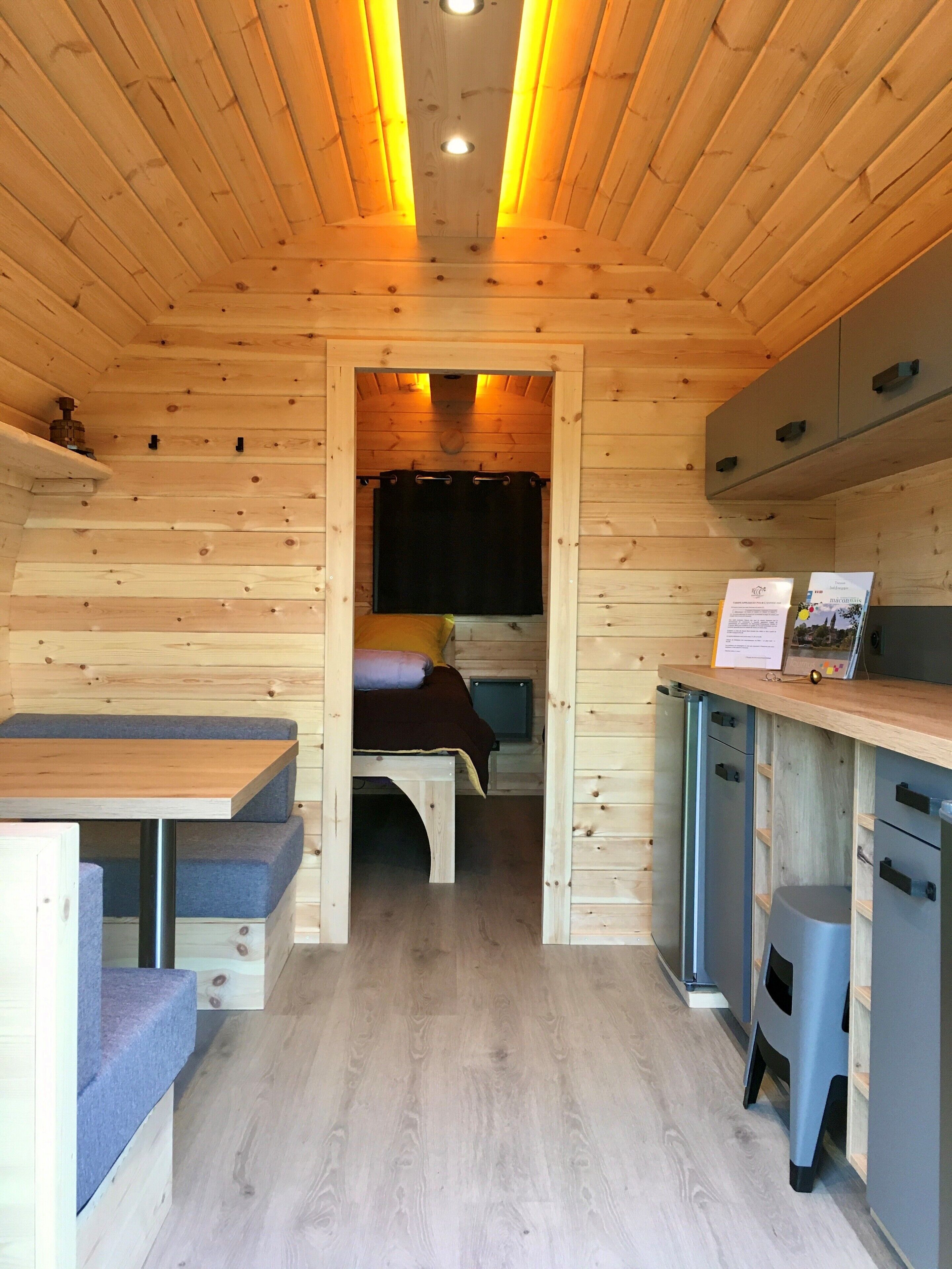 Une petite cabane en bois comprenant un coin cuisine, un lit et un petit espace repas.