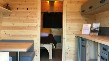 Une petite cabane en bois comprenant un coin cuisine, un lit et un petit espace repas.