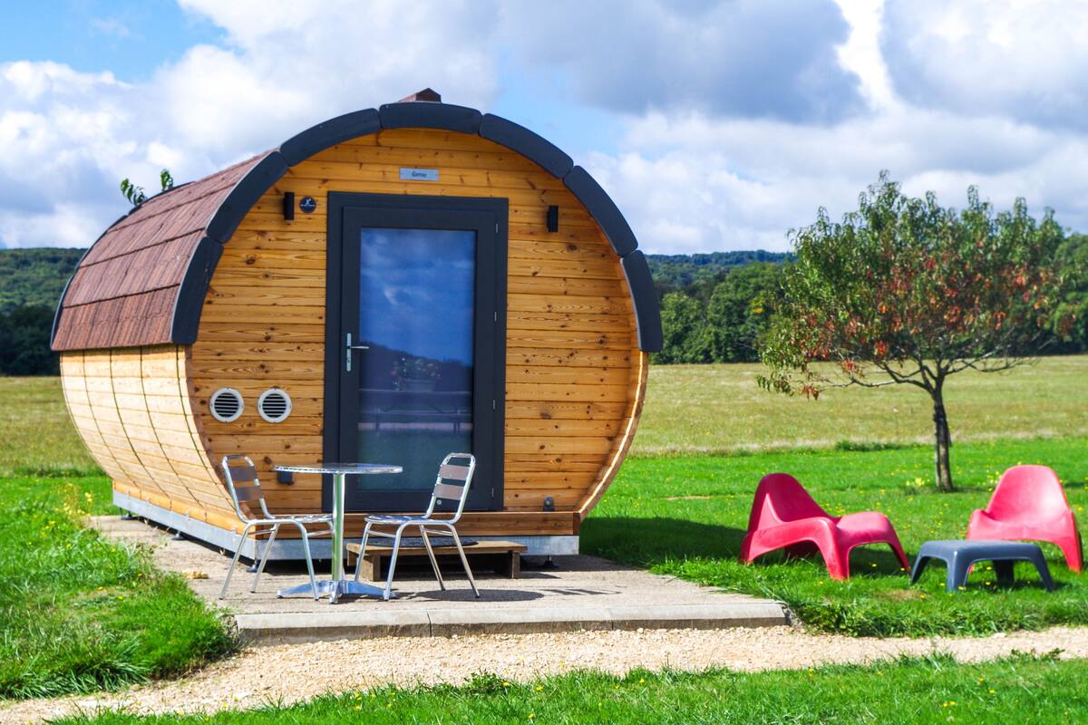 A wooden cabin with a curved roof, a door, and a window. There is a table and two chairs outside.