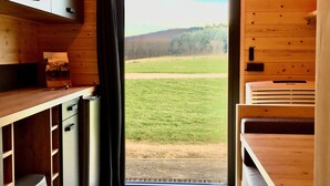 A compact kitchen with wooden cabinets, a countertop, and a view of a grassy field through a door. - Domaine Joseph LAFARGE Wine Resort Oeno-tonneaux expérience (Lugny)