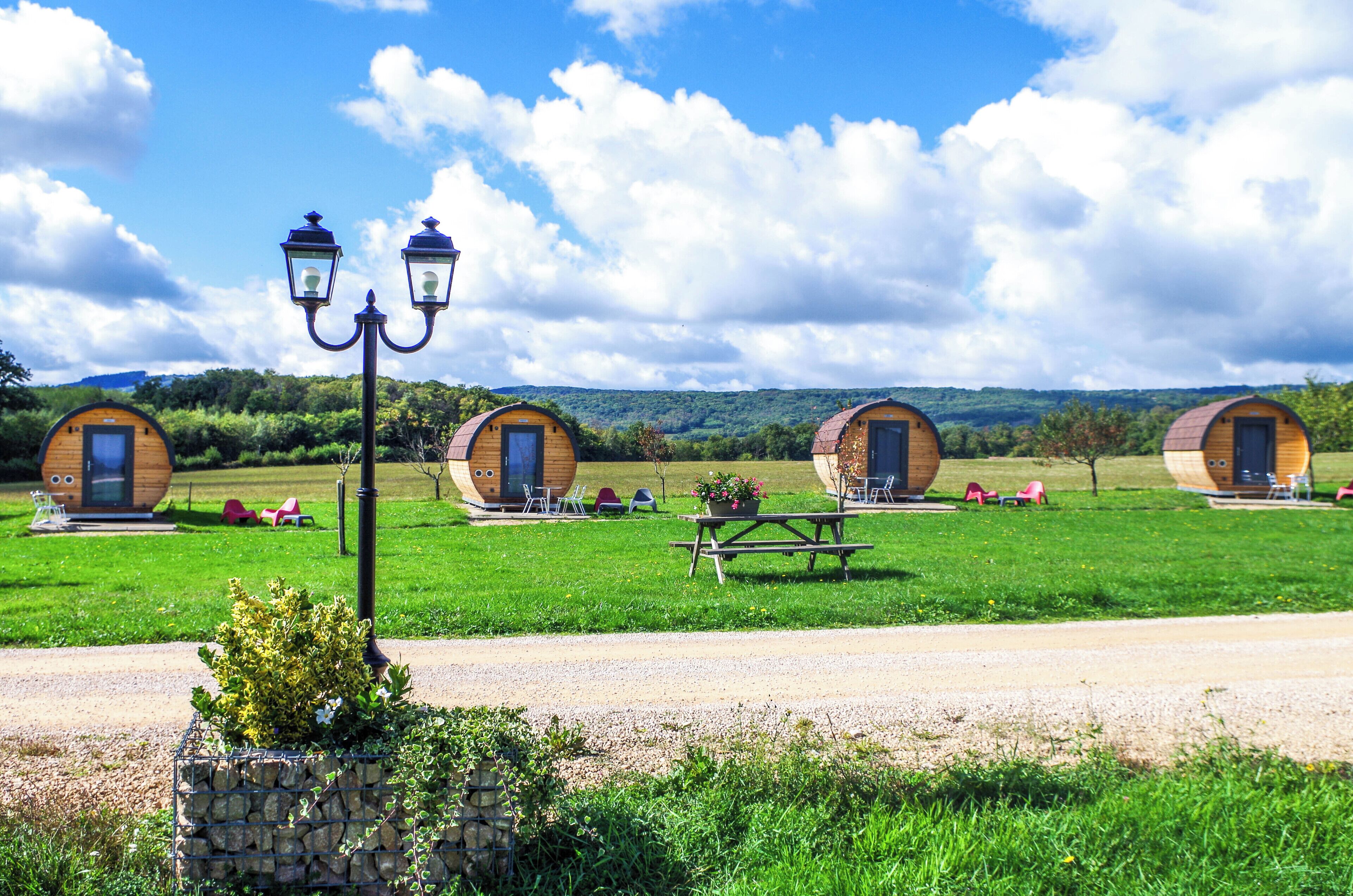 Drie ronde houten hutten met deuren, een picknicktafel en een lantaarnpaal in een grasveld.