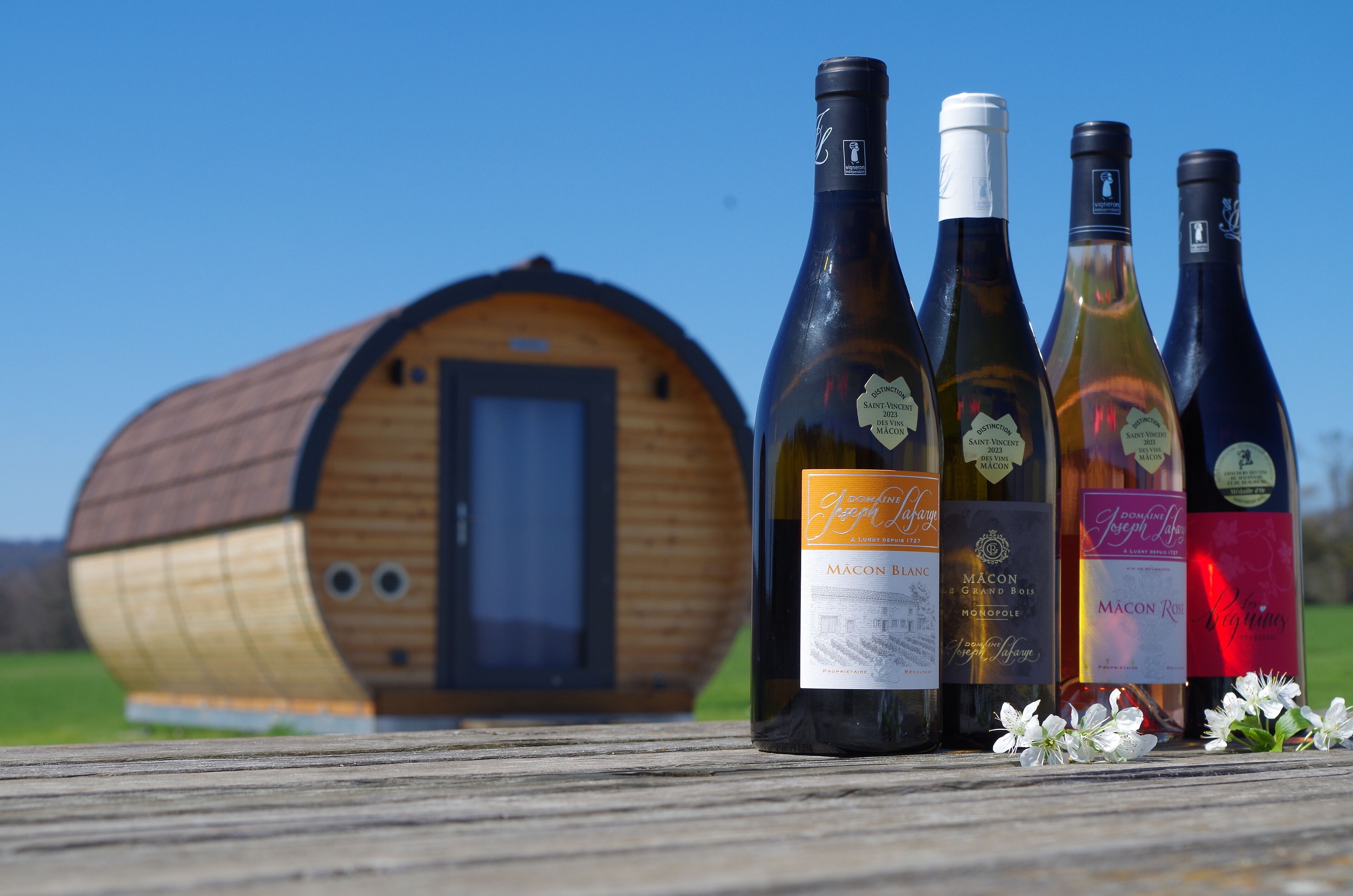 Four wine bottles with labels in front of a wooden barrel-shaped building.