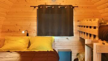 L’intérieur d’un chalet accueillant, avec un plafond en bois, un lit recouvert d’une couverture marron foncé, une petite table de chevet et un lit superposé en bois.
