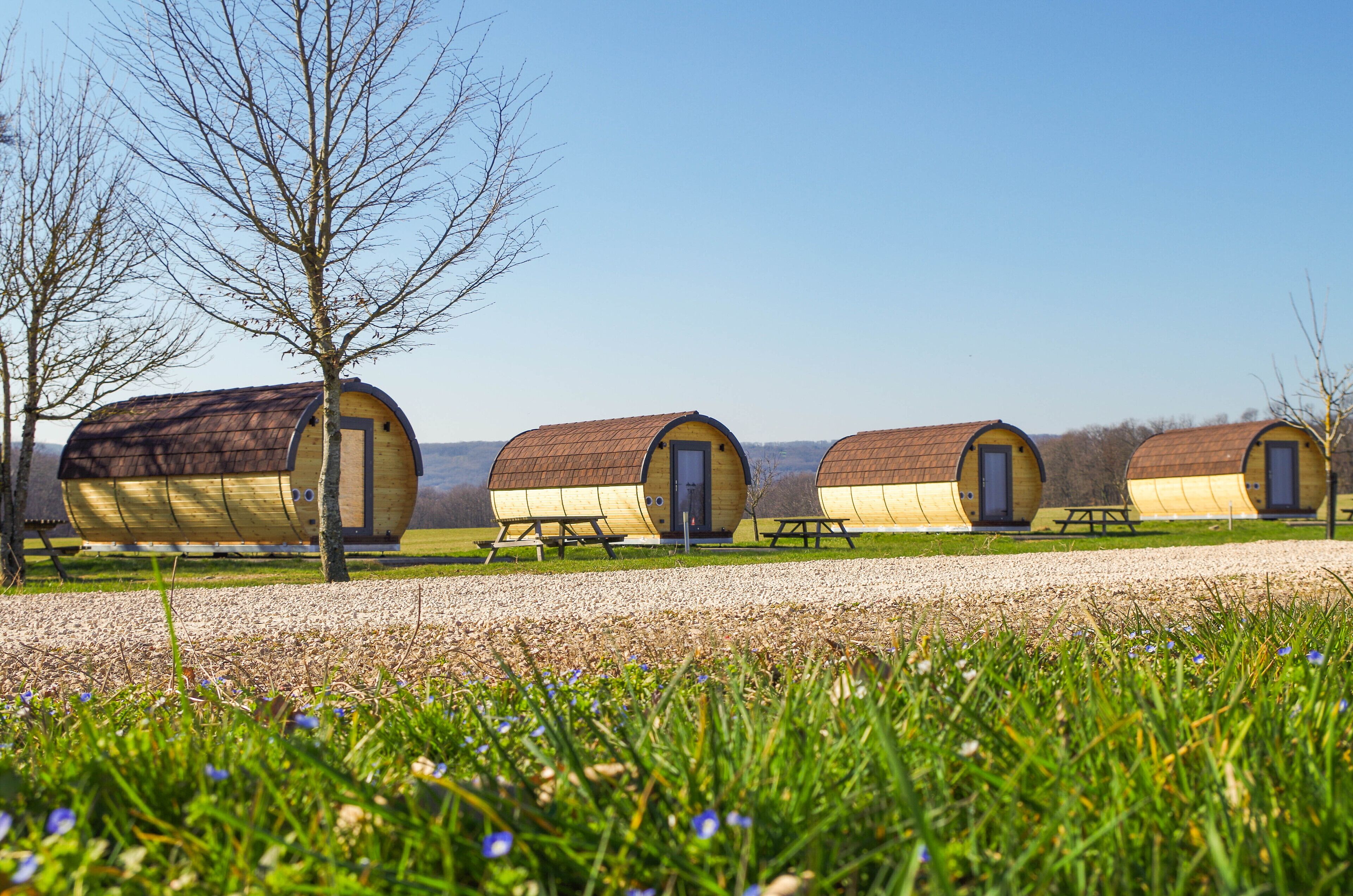 Une rangée de cabanes cylindriques avec des tables de pique-nique, installées dans un champ verdoyant.