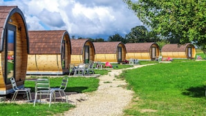 Une rangée de cabanes en bois aux toits en arc de cercle, chacune dotée d’une porte et d’une fenêtre, et un chemin de gravier menant à ces cabanes.