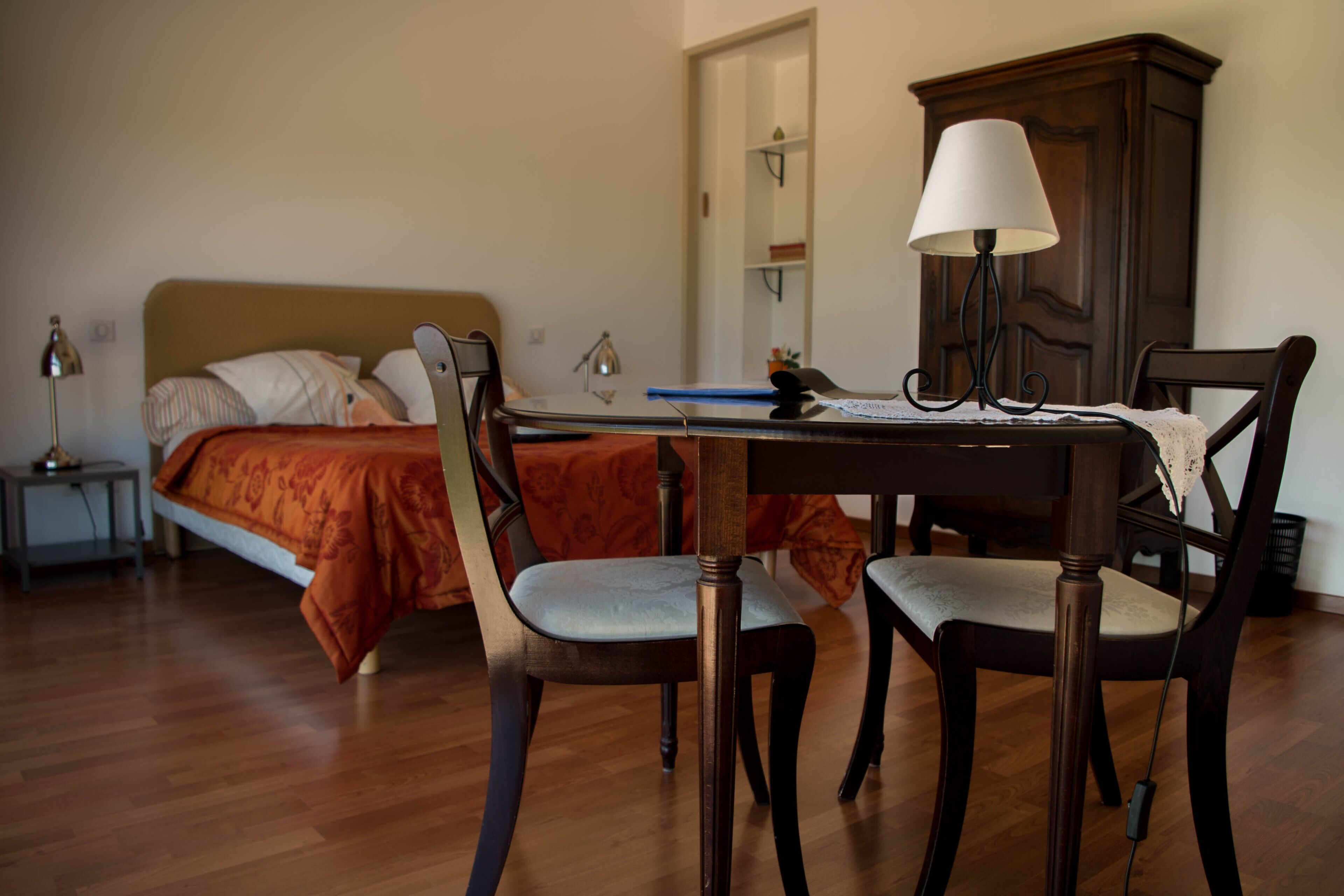 Un dormitorio con cama, mesita de noche, escritorio con lámpara y una silla.
