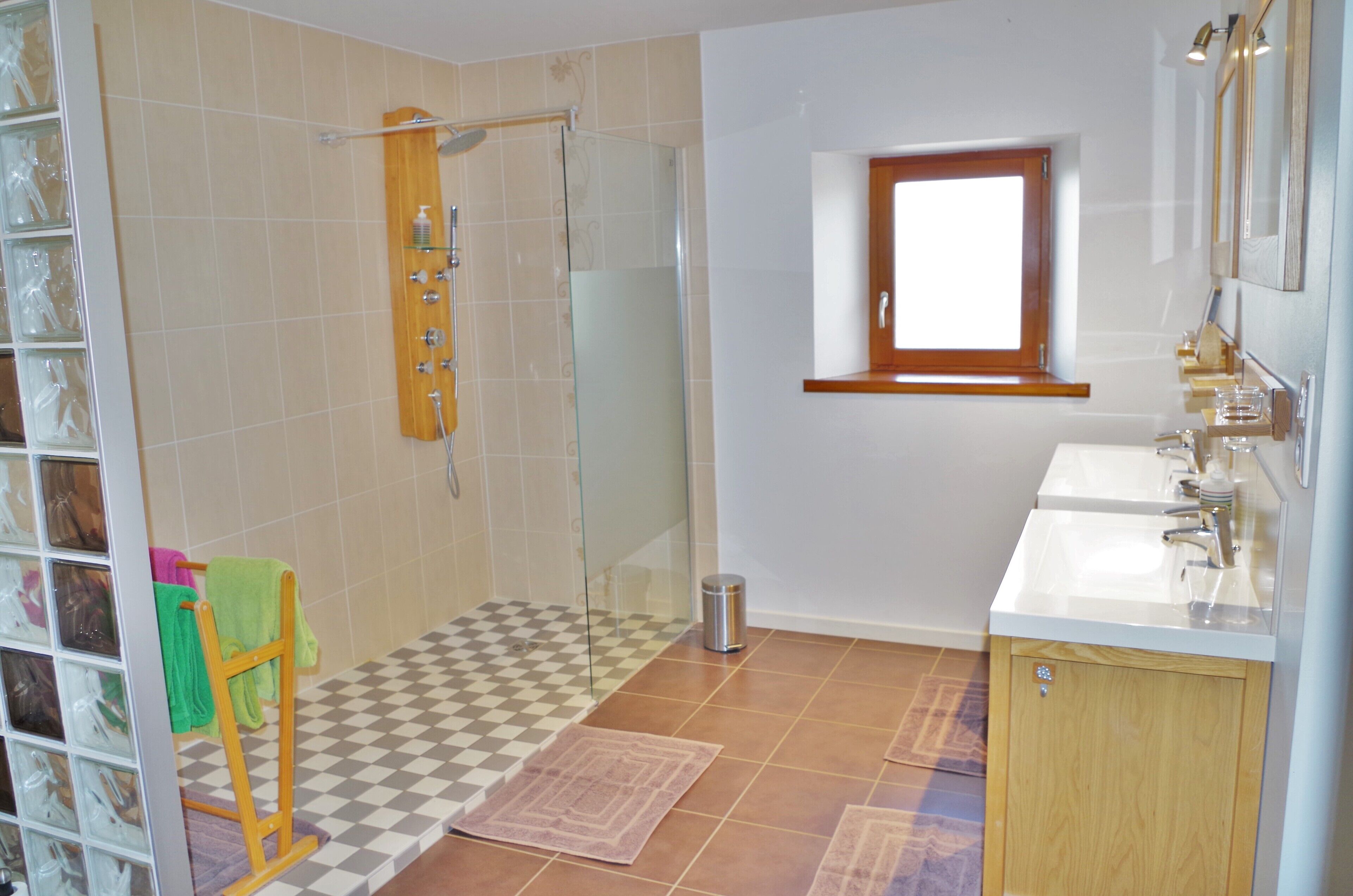 A bathroom with a glass shower enclosure, a sink with a mirror, and a window above the sink.