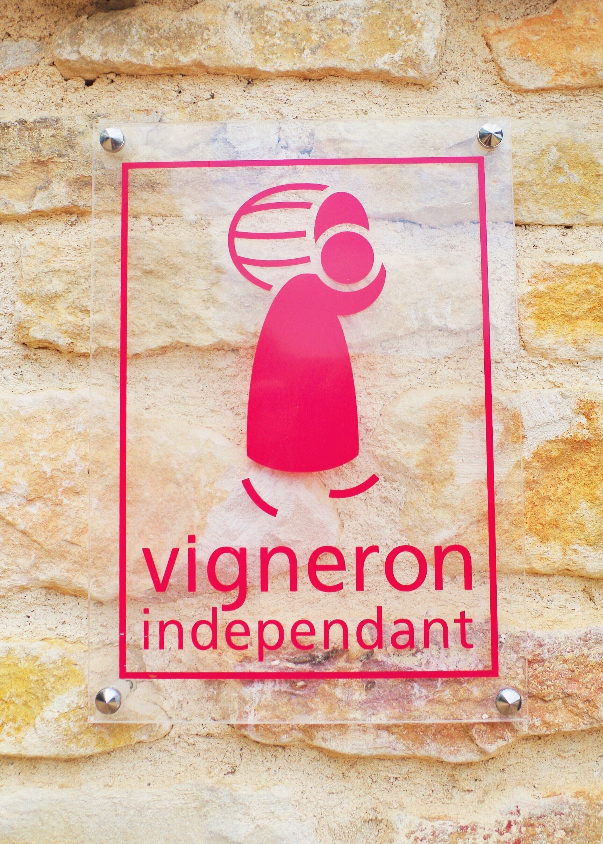 Een bord met een gestileerde figuur en de tekst 'vigneron independent' op een stenen muur.