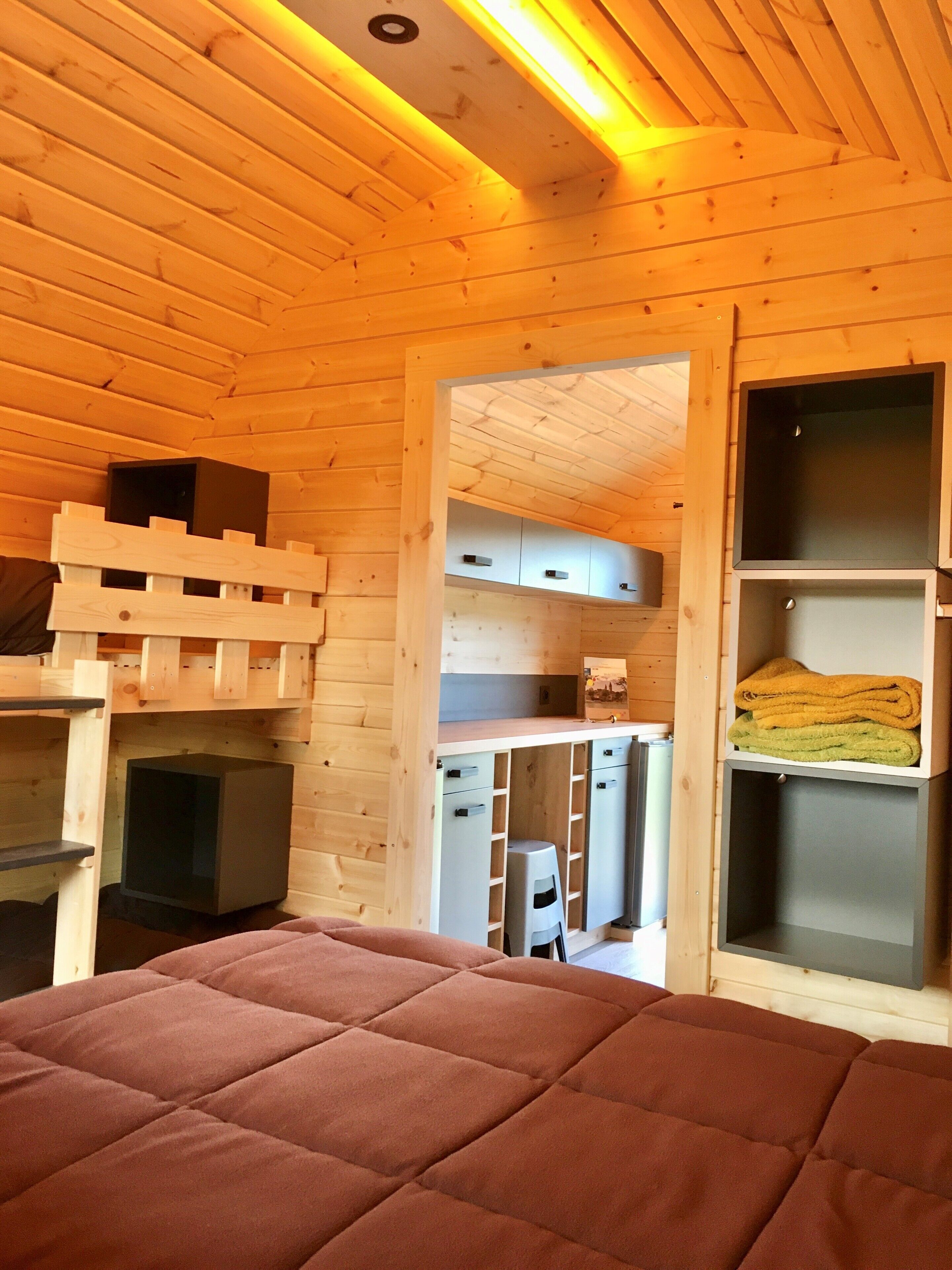 A cozy wooden cabin interior with a bed, built-in storage, and a kitchenette.