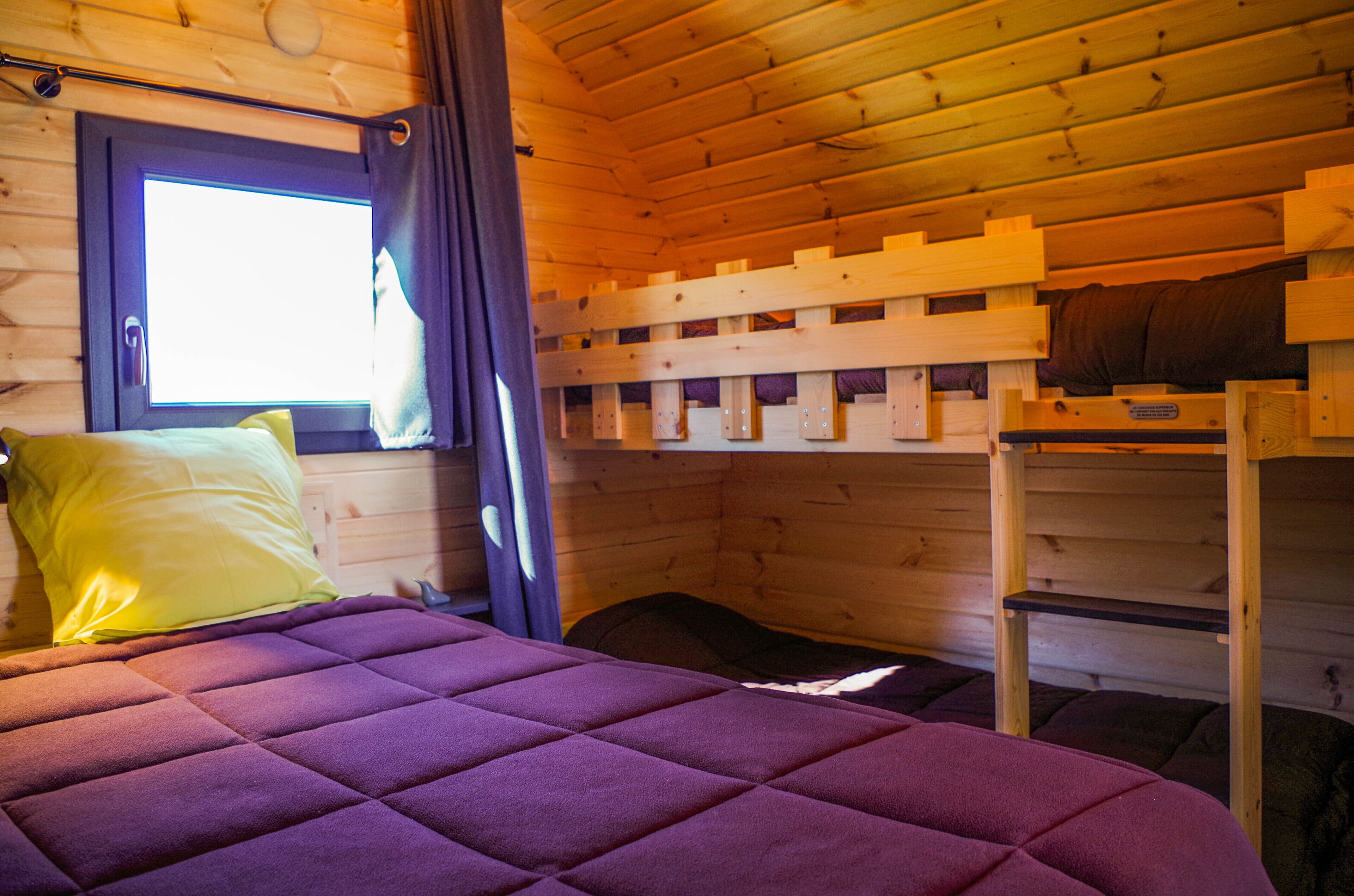 Una camera in una baita di legno con un letto, letti a castello e una finestra con tende.