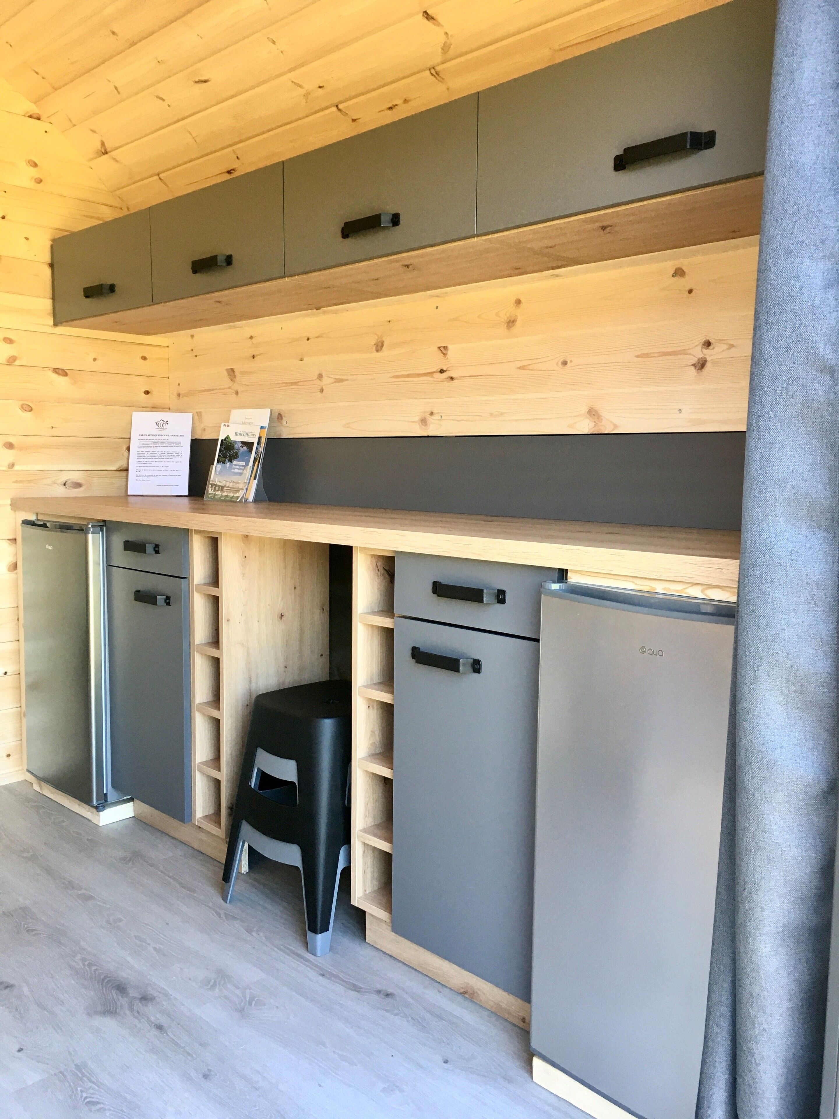 Een compacte keuken met houten kastjes, een klein krukje en een koelkast.