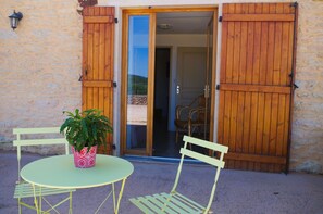 Un espace extérieur aménagé avec une table et des chaises, un pot de fleurs et des volets en bois sur un mur de pierre.