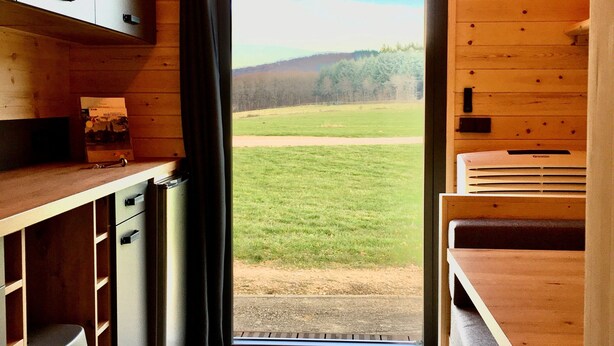Une cuisine de taille réduite, avec des meubles en bois, un plan de travail et une vue sur un champ verdoyant par une porte.