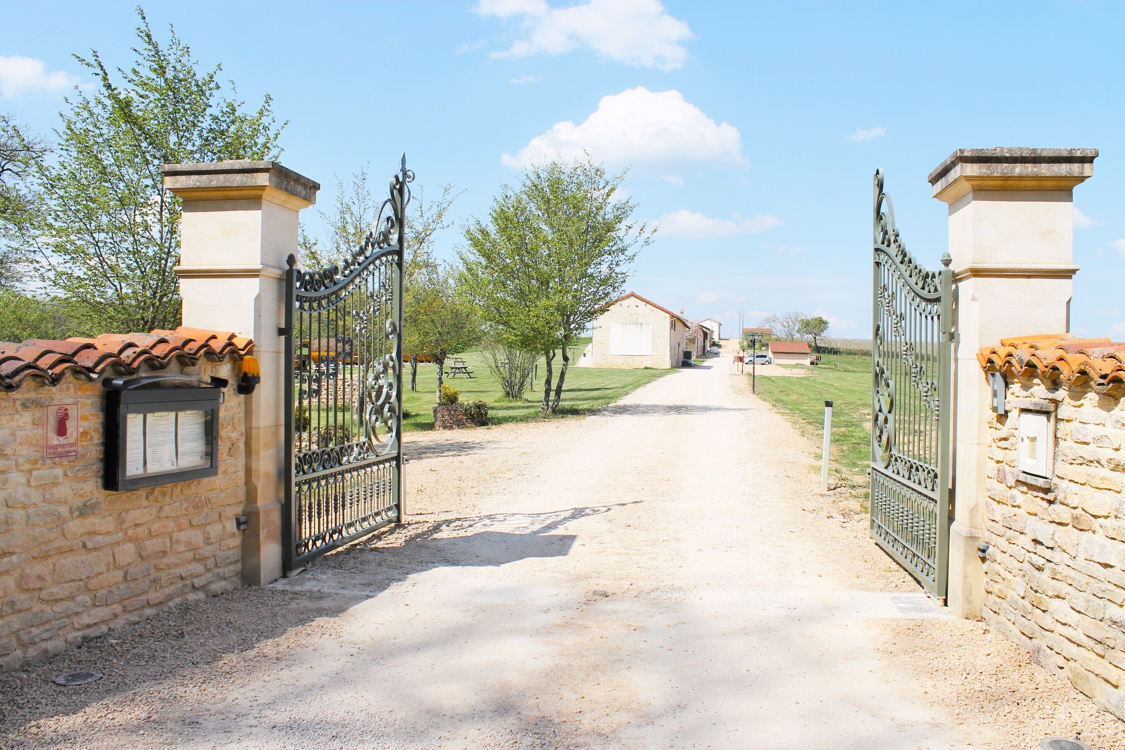A gated entrance with a gravel path leading to a building with a tiled roof.