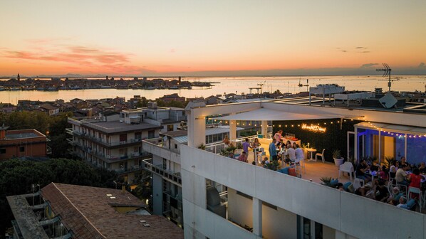 Un bar situé sur le toit d’un immeuble, offrant une vue sur la ville et l’eau au coucher du soleil.