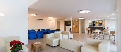 A spacious living area with a high ceiling, a kitchen in the background, and a seating area with sofas and chairs.
