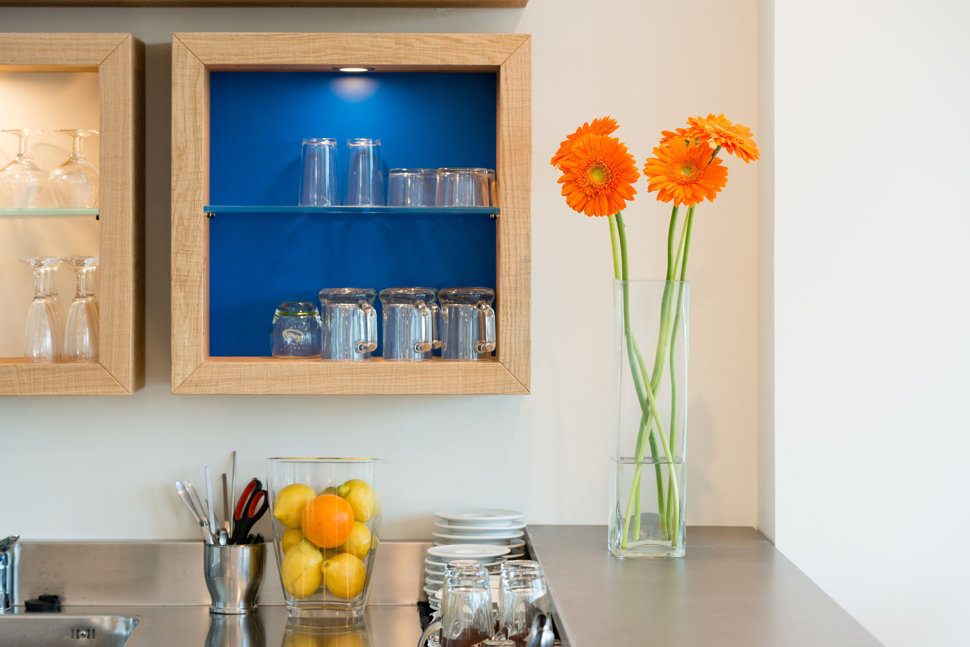 A kitchen counter with glassware, a fruit bowl, and a vase with flowers.