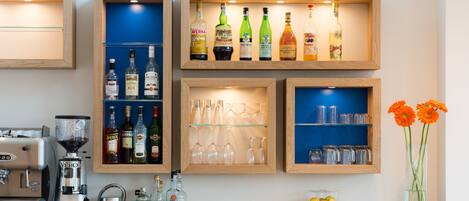 Zona de bar con estantes llenos de botellas de licores, vasos y una máquina de café.