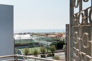 Vue d’un complexe sportif comprenant un grand stade et des courts de tennis, surplombant une plage et la mer.