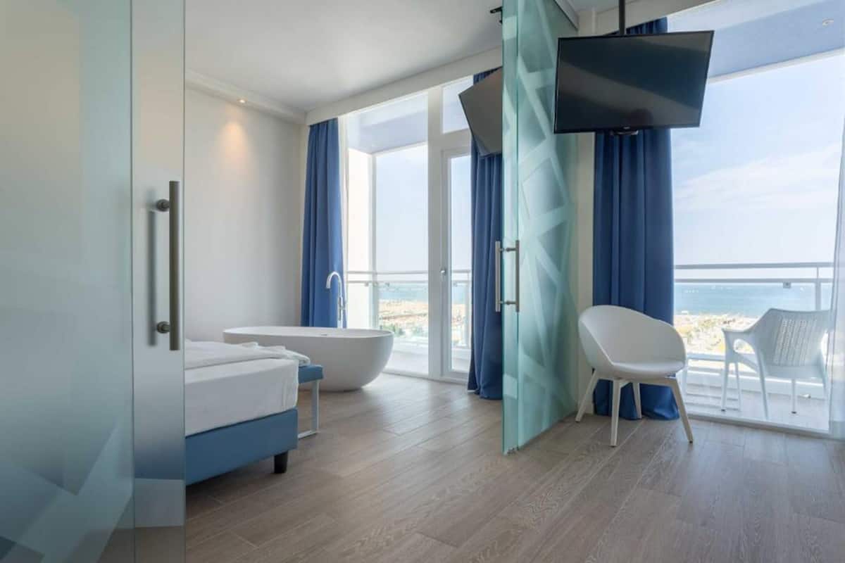 Une salle de bain moderne dotée d’une baignoire, d’une douche et d’une grande fenêtre offrant une vue sur la mer.