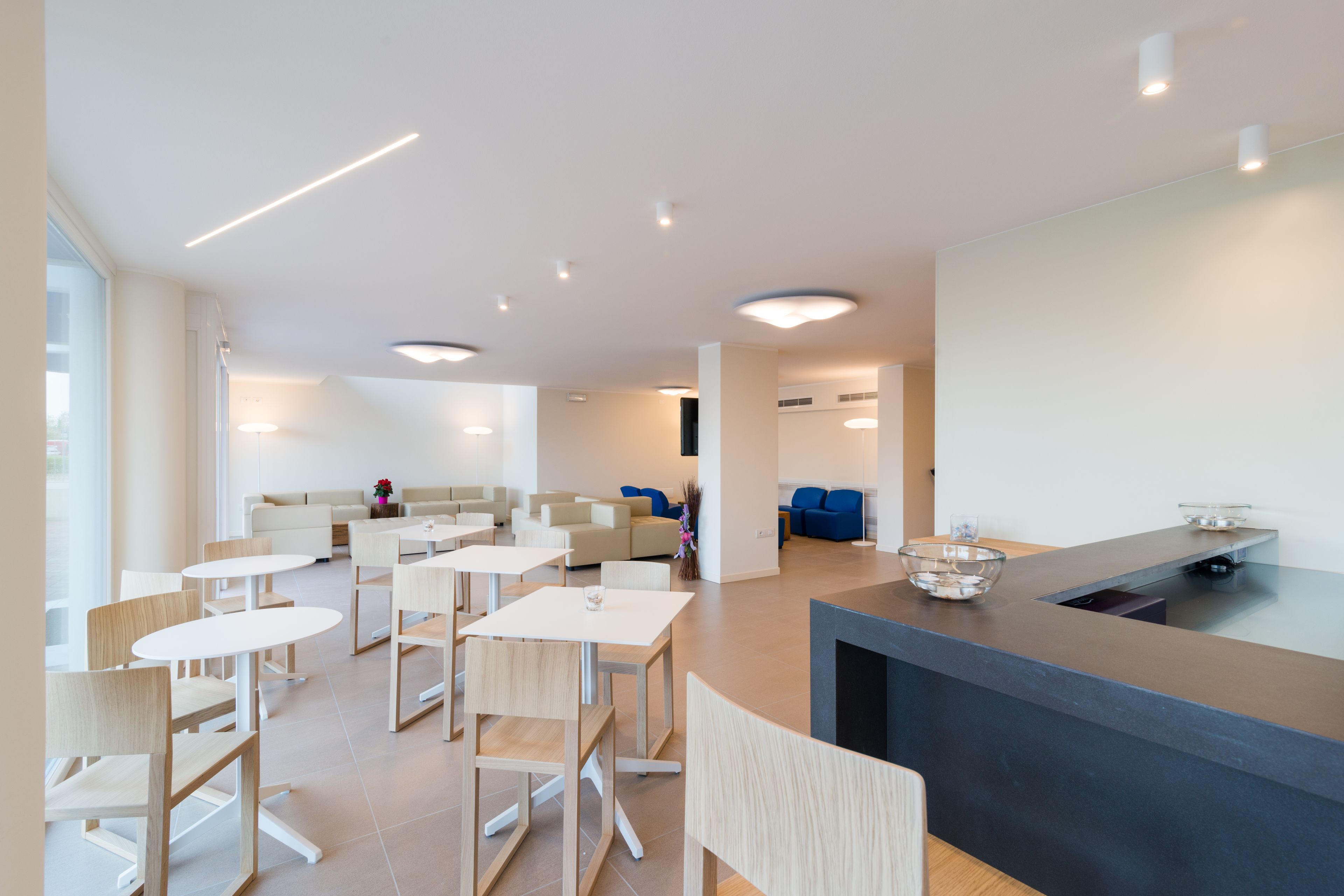 Un área de comedor moderna con mesas y sillas redondas, un mostrador de recepción y una sala de estar con sofás.