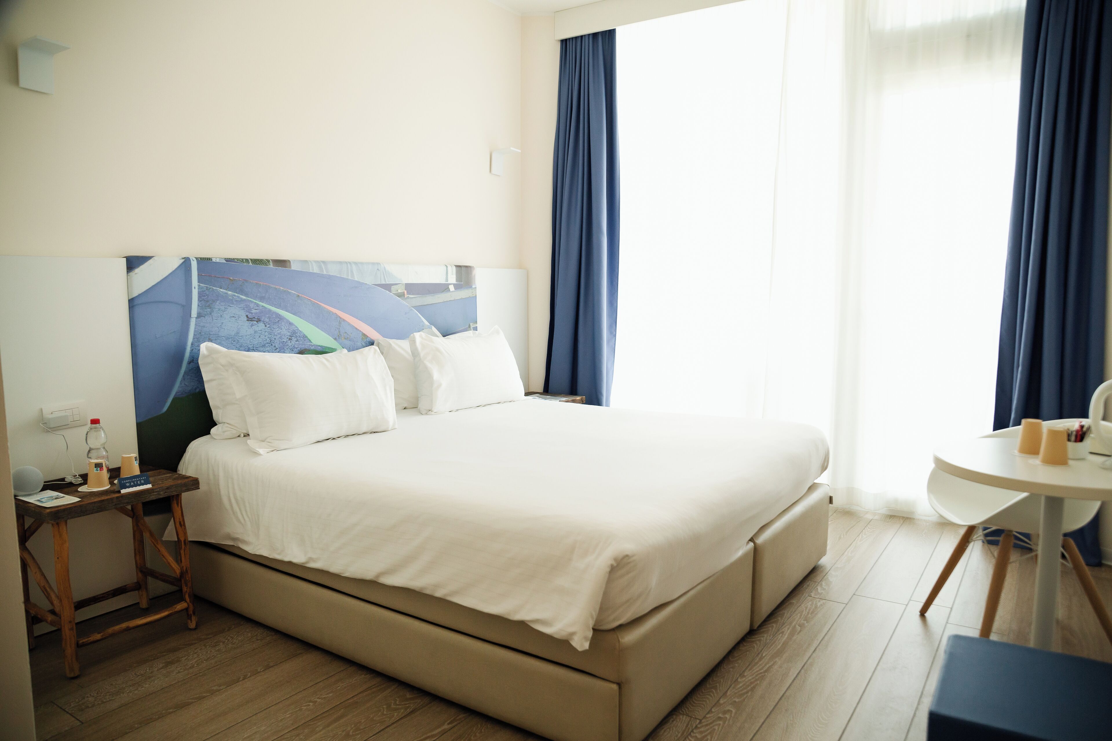 Ein Hotelzimmer mit einem großen Bett, einem kleinen Tisch mit zwei Tassen, einem Nachttisch und einem Bild an der Wand.