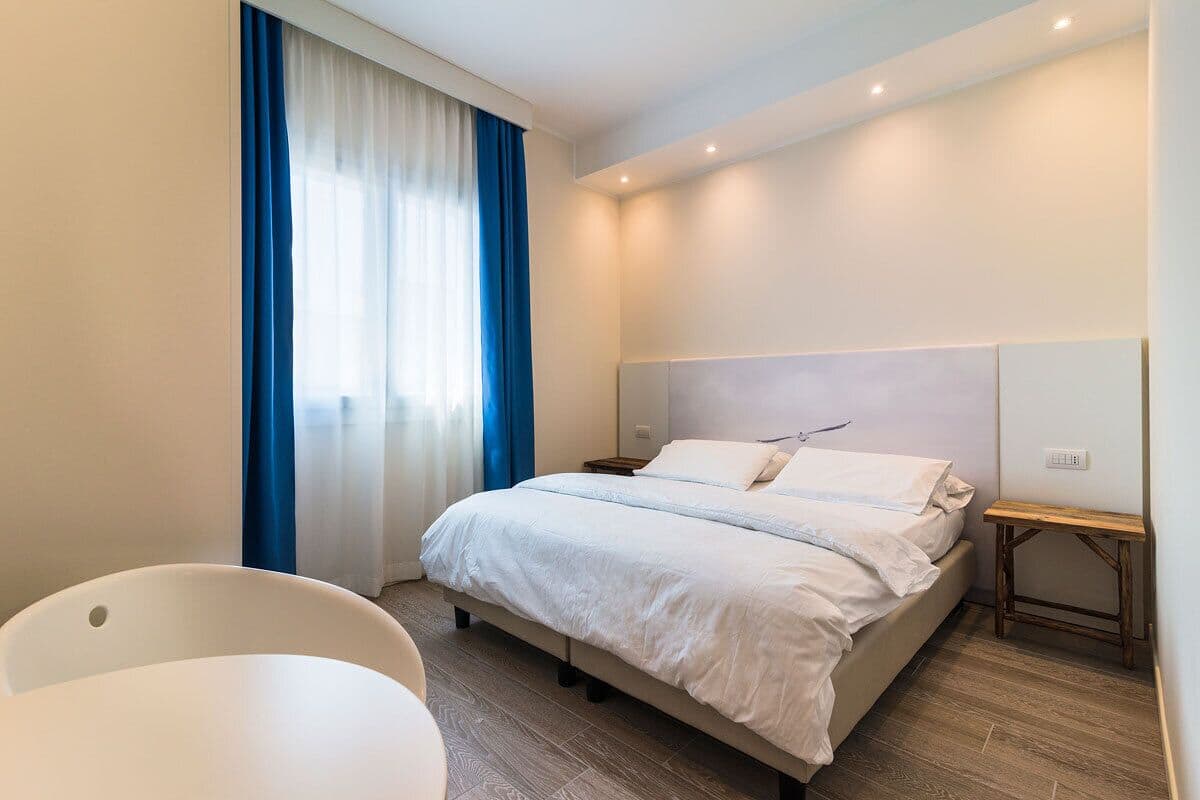 Une chambre d’hôtel moderne avec un grand lit, une table de chevet, une chaise et une fenêtre avec des rideaux.
