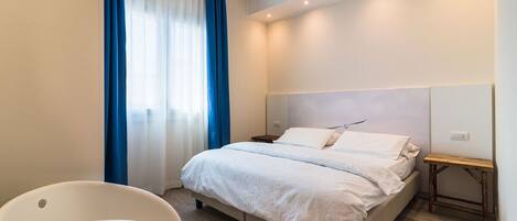 Una habitación de hotel moderna con una cama grande, una mesita de noche, una silla y un ventanal con cortinas.