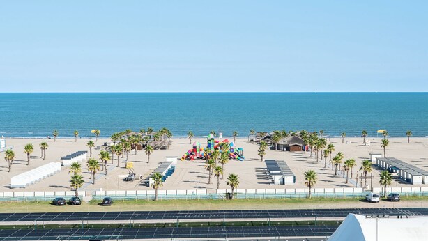 A beach with palm trees, a playground, and a parking area with solar panels. - Smart Hotel Mediterraneo (Chioggia)