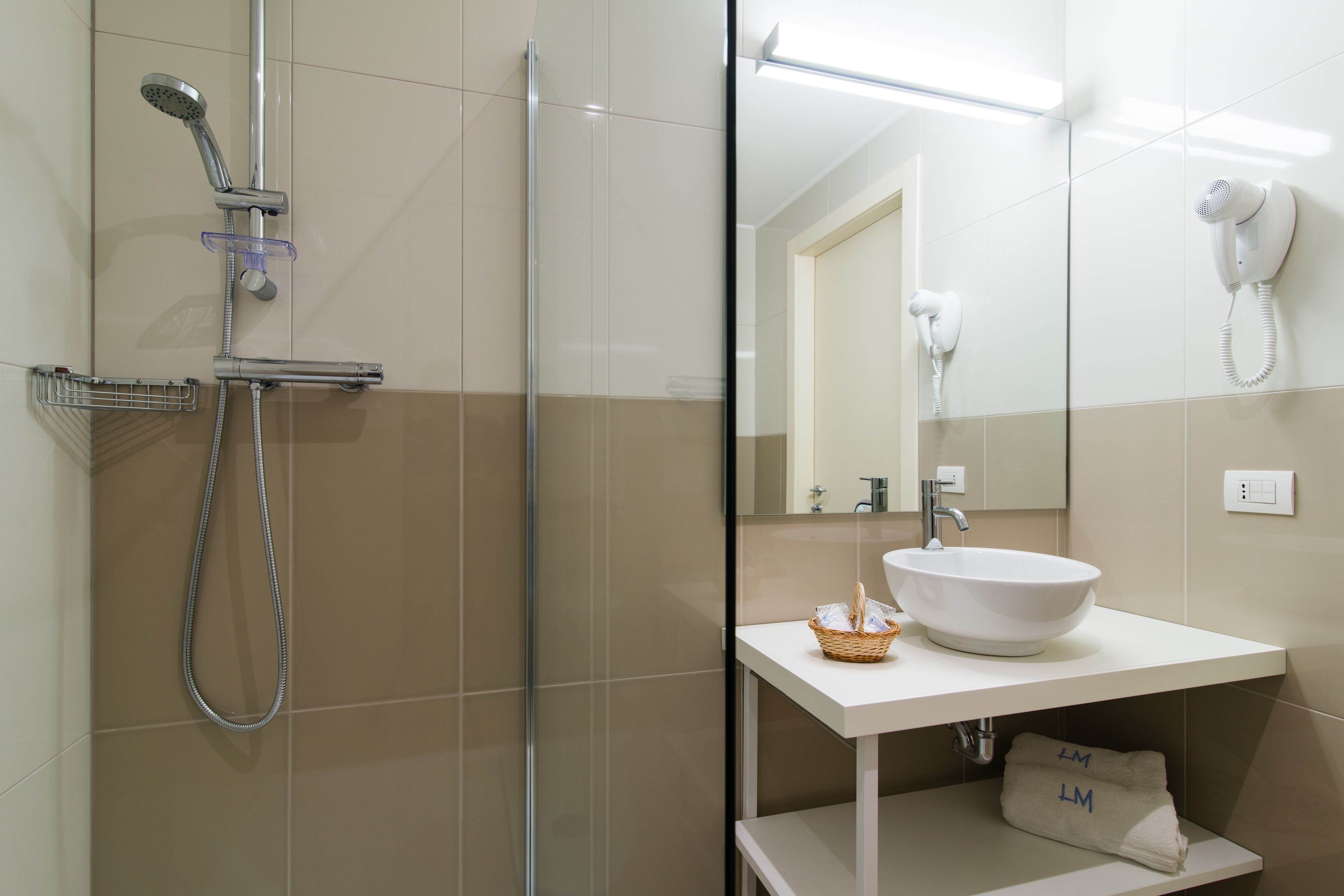 A modern bathroom with a glass-enclosed shower, a white sink, and a hairdryer mounted on the wall.