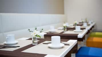 A dining area with multiple tables set with white cups, plates, and cutlery.