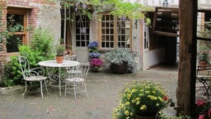 A courtyard with a brick wall, a wooden pergola, a round table with chairs, and potted plants. - A l'Ecole Buissonnière (Honfleur)