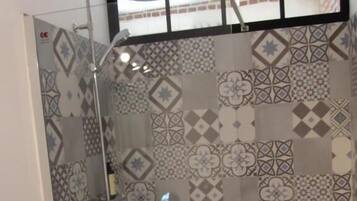 A shower with a glass door and a view of a building outside.