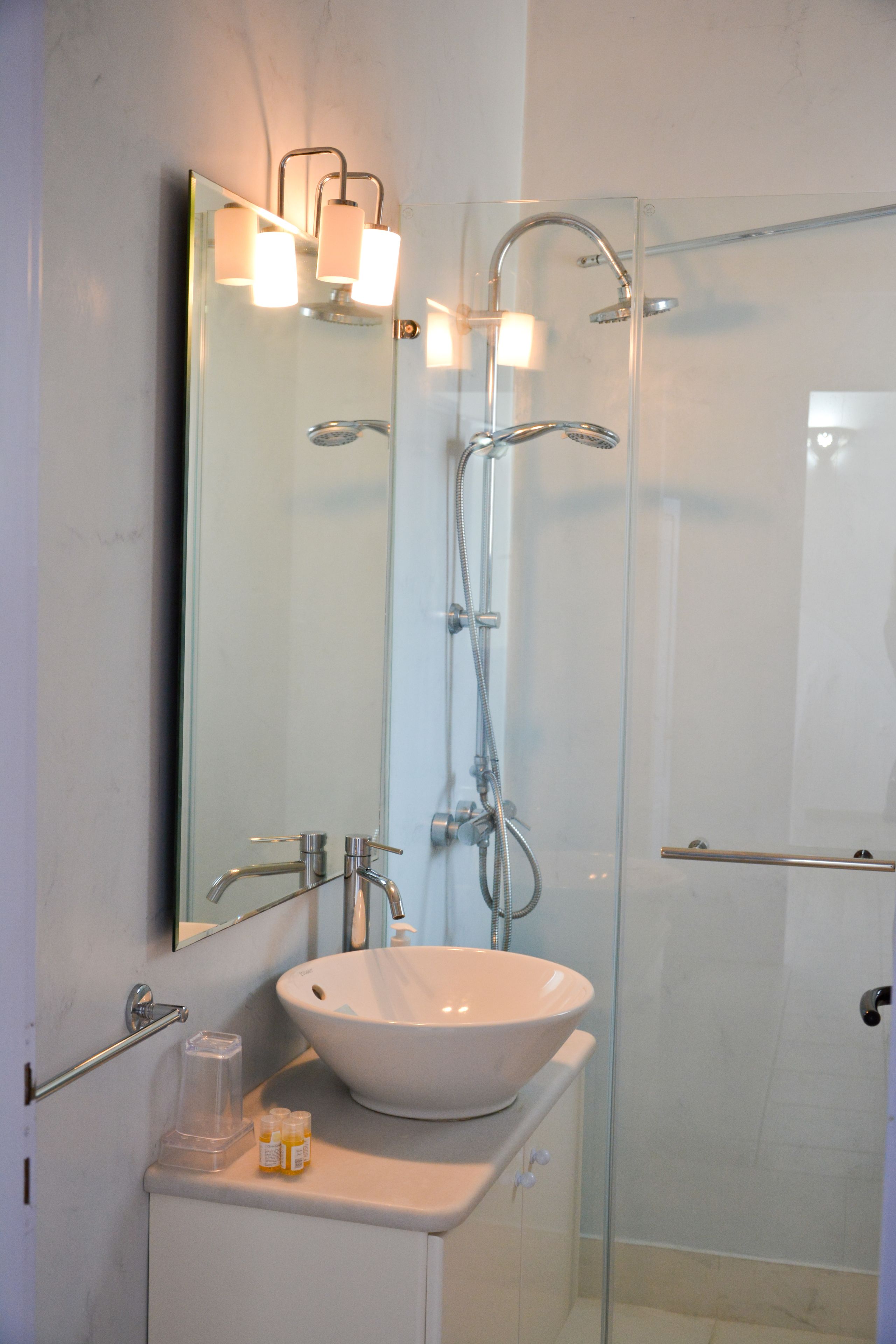 A modern bathroom with a glass-enclosed shower, a white sink, and a mirror with wall-mounted lights.