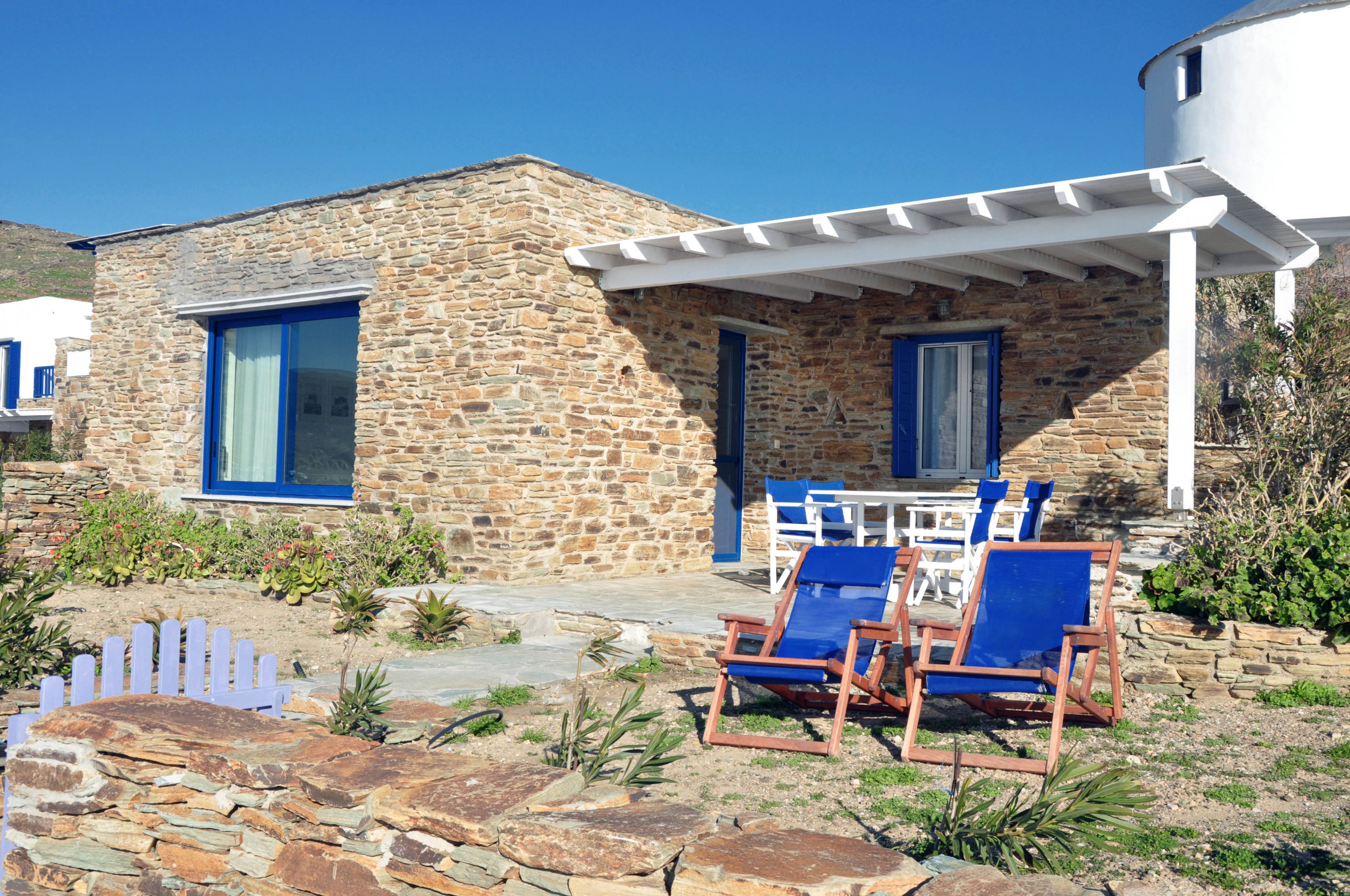 Un edificio in pietra con un portico bianco e finestre con cornice blu. Due poltrone blu e un tavolo con sedie sono all'esterno.
