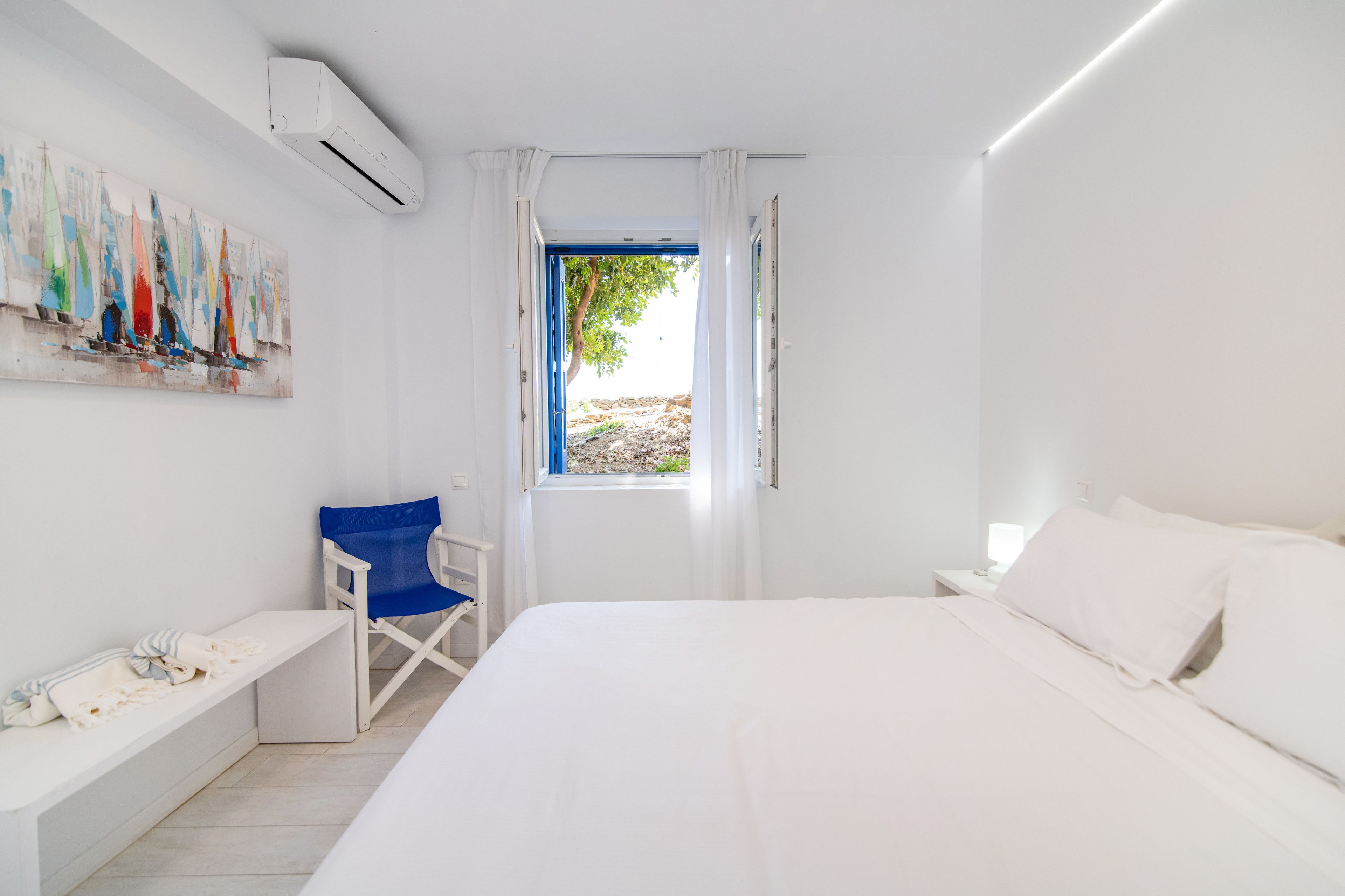 Een slaapkamer met een groot bed, een stoel, een bankje en een raam met gordijnen.