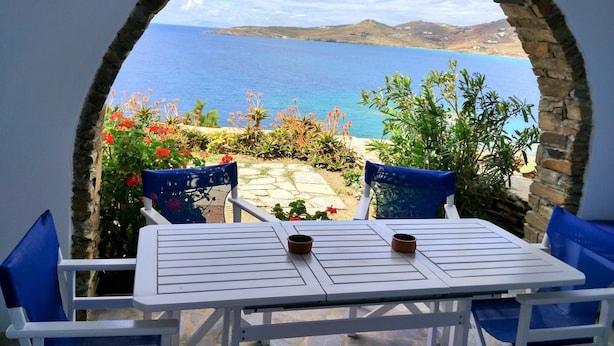 A table and chairs set up under a stone archway with a view of the sea and hills. - Stavros Bay (Tinos)