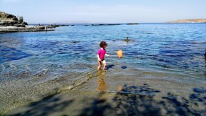 A child playing in shallow water near a rocky shoreline. - Stavros Bay (Tinos)