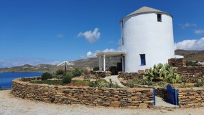 A white windmill with a stone pathway leading to a covered entrance, surrounded by cacti and a clear blue sky. - Stavros Bay (Tinos)