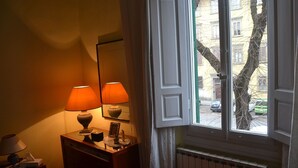 A room with a wooden dresser, two lamps, a mirror, and a window with open shutters. - La Rosa di Firenze (Florence)