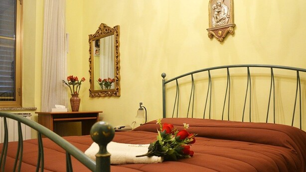 A bedroom with a bed, a bedside table, a mirror, and a wall-mounted decoration. - La Rosa di Firenze (Florence)