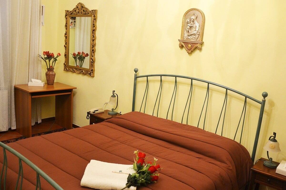 A neatly made bed with a brown bedspread, a bedside table with a lamp, a mirror, and a small statue on the wall.