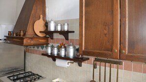 A kitchen with wooden cabinets, a gas stove, and shelves holding kitchenware. - La Rosa di Firenze (Florence)