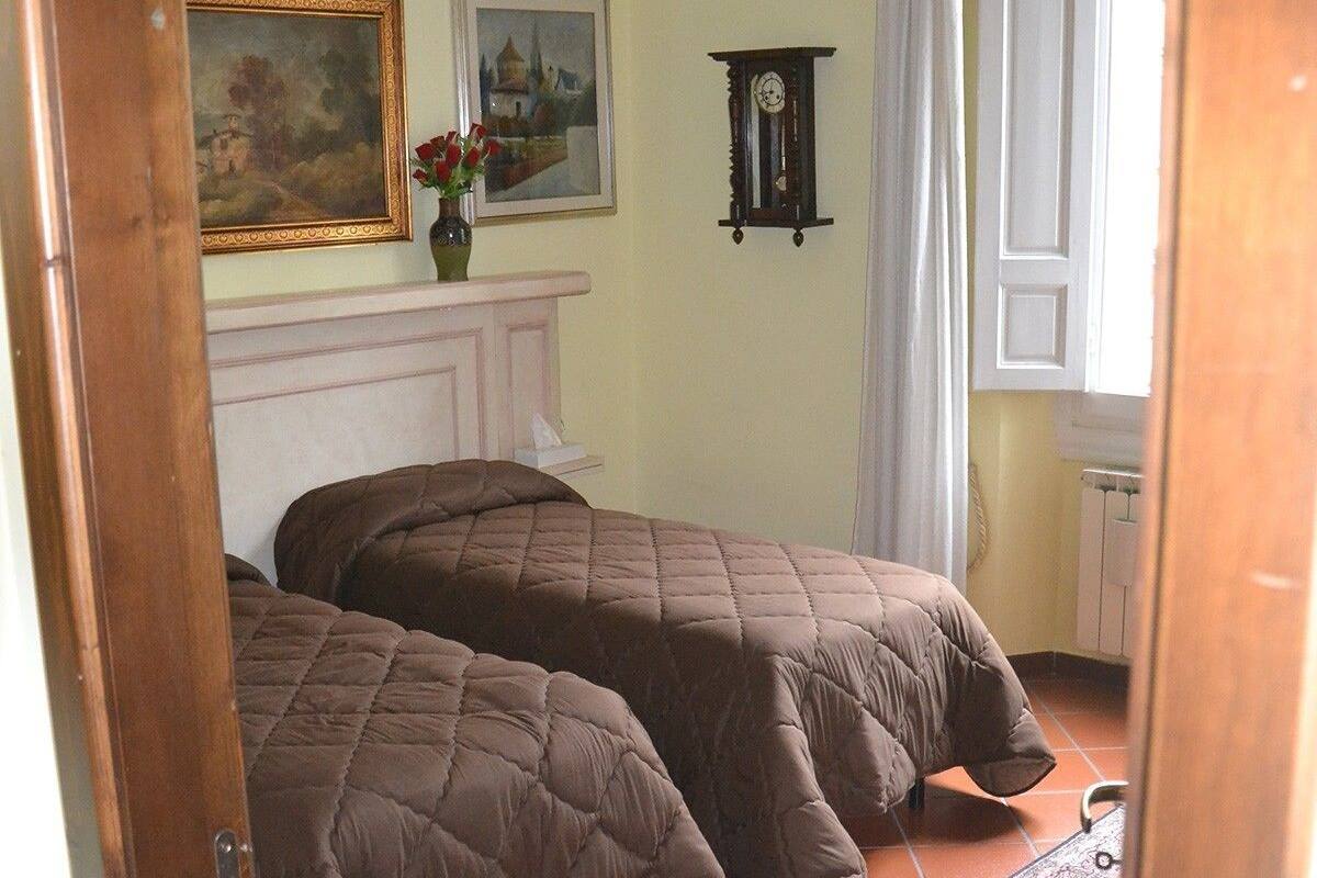 A bedroom with two beds, a fireplace, a clock, and two paintings on the wall.