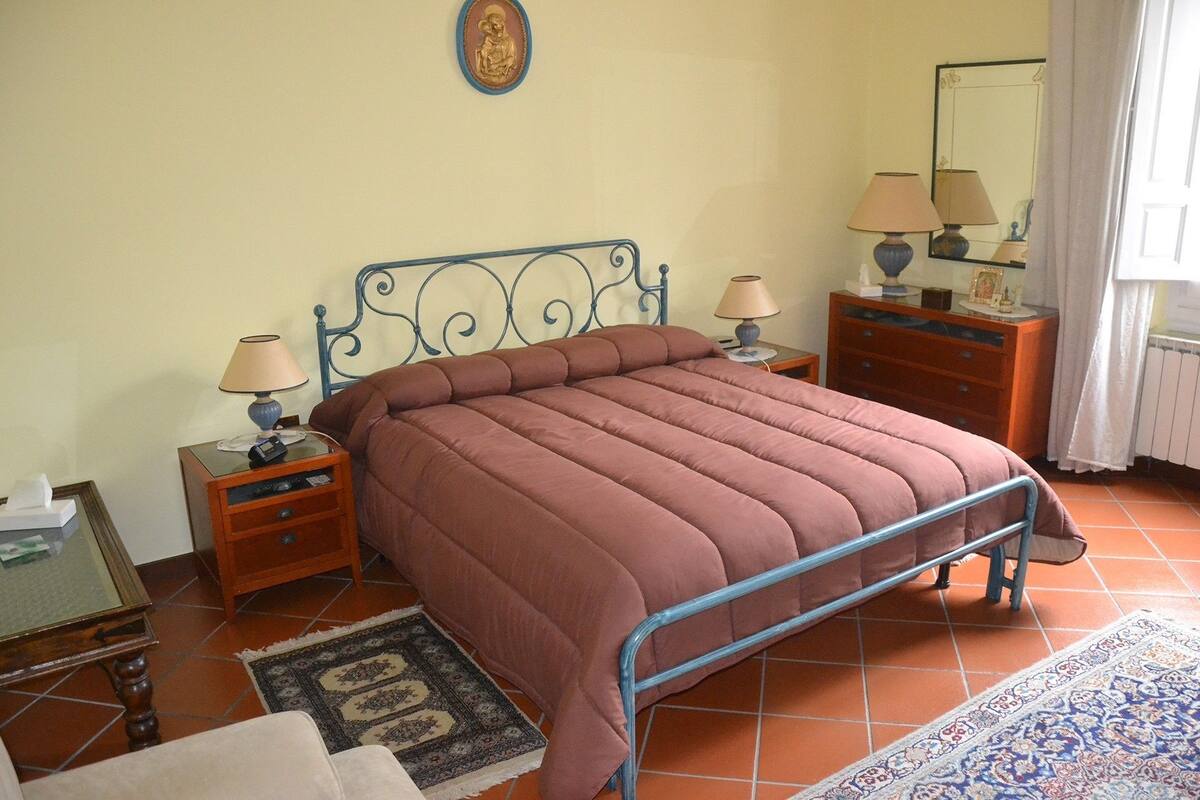 A bedroom with a bed, two bedside tables, a dresser, a mirror, and a patterned rug.