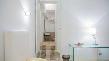 A bedroom with a bed, a glass table with a lamp, and a staircase leading to a bathroom.