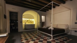 Un dormitorio con suelo a cuadros, una cama con dosel, una bañera junto a una pared de piedra y vistas a través de un arco.