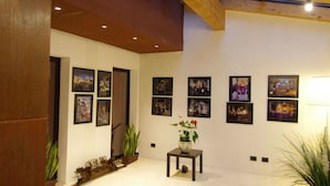 Una galería con fotografías enmarcadas en las paredes, una mesa pequeña con un florero y plantas en macetas.