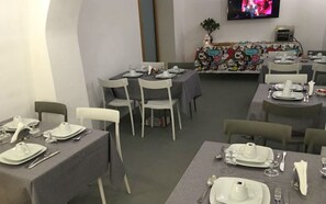 A dining area with tables set for meals, chairs, a television screen, and a colorful table runner.
