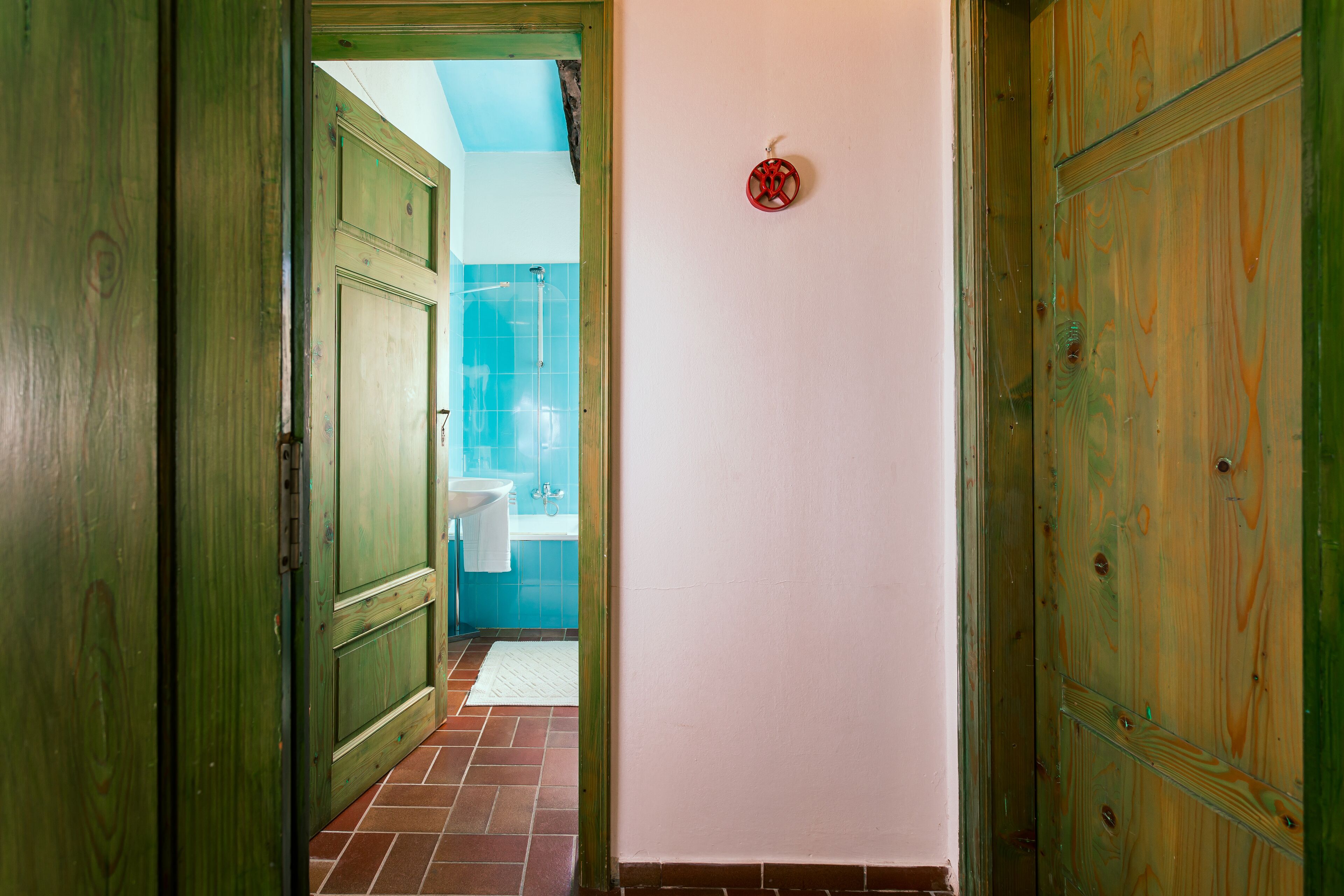 A hallway with wooden doors, a tiled floor, and a bathroom with blue tiles and a white sink.